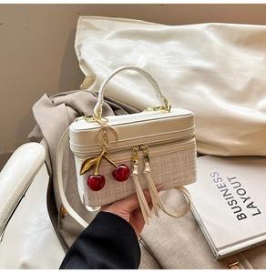 Close-up of ivory tweed and leather crossbody bag with cherry charm and top handle