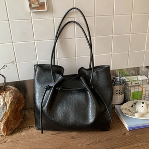 Close-up of black tote bag with vintage wrinkled texture and drawstring detail on wood