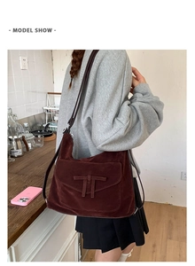 Brown suede shoulder bag with T-shaped ornament shown in a casual lifestyle setting