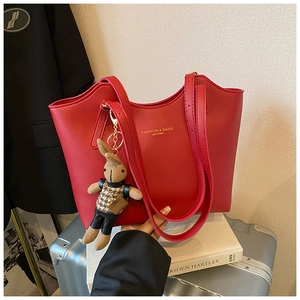 Détail d'un sac cabas en cuir rouge avec un charme de lapin sur une valise argentée