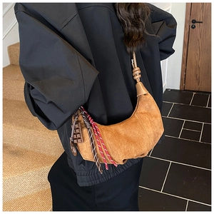 Détail du sac croissant en daim caramel avec bandoulière tressée et accents de glands rayés