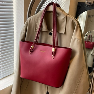 Close-up of red leather tote bag with gold logo and straps against a beige coat