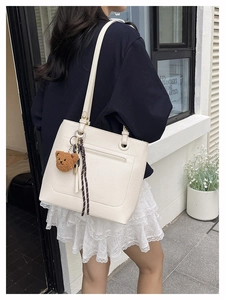 Detail of white pebbled leather tote bag with long strap and cute teddy bear pendant