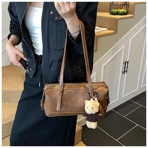 Close-up of retro brown leather cylinder bag with textured finish and cute bear charm