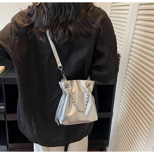 Close-up of shiny silver bucket bag featuring metallic chain and drawstring closure