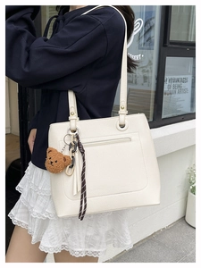 Detail of cream white tote bag with pebble leather texture and a cute bear charm