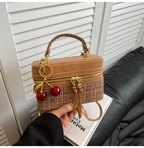 Detail of warm brown leather and woven texture handbag with cherry pendant decoration
