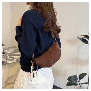 Detail of a brown suede half-moon crossbody bag featuring a beaded fringe tassel charm