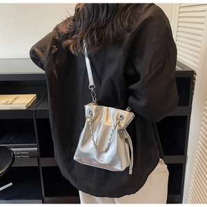 Close-up of metallic silver drawstring bucket bag with chain detail on a model