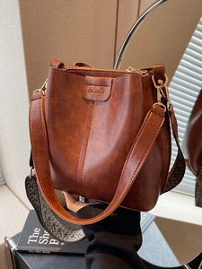 Retro caramel brown bucket bag with wide woven strap and polished gold hardware details