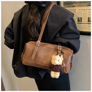 Close-up of vintage brown shoulder bag with cute teddy bear charm on textured leather
