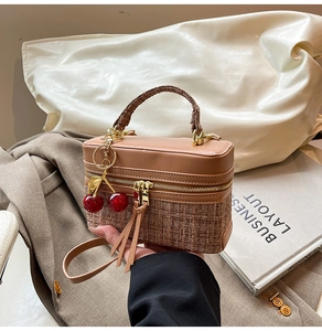 Close-up of brown textured tweed and leather handbag with a red cherry charm detail