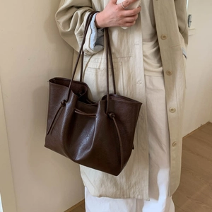 Detail of dark brown leather tote bag featuring stylish side knots and long shoulder straps