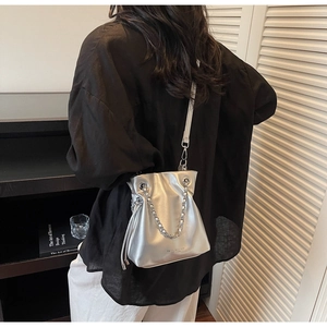 Fashionable silver metallic bucket bag worn by model, featuring chain handle and strap