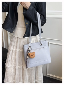 Detail view of light purple leather tote bag with brown plush bear charm accessory