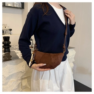 Detail of brown suede croissant bag with leather strap and decorative beaded tassel charm