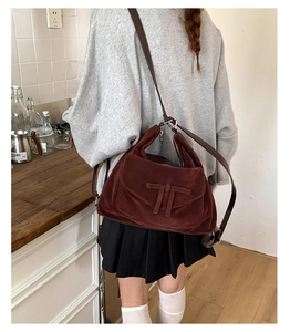 Detail view of burgundy suede flap shoulder bag with unique T-shaped trim on model