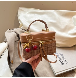 Close-up of retro box handbag with brown leather stitching and cherry pendant