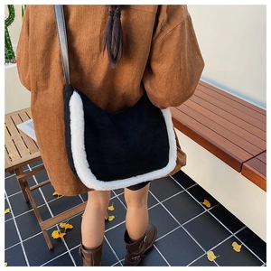 Detail view of black suede shoulder bag with white faux fur trim and leather strap