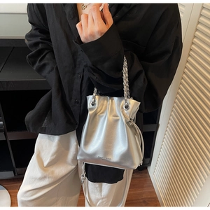 Detail of silver metallic bucket bag with woven chain handle and textured faux leather