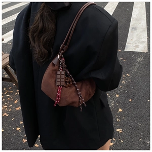 Détail du sac demi-lune en daim marron foncé avec breloque chocolat et pendentif tressé