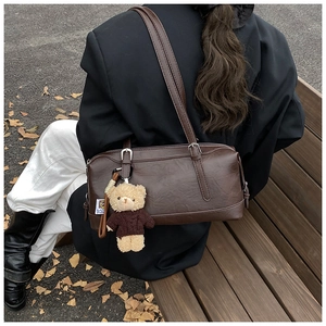 Detail view of a vintage dark brown barrel bag with a cute bear plush charm outdoors