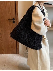 Large black plush tote bag with leather strap, warm interior background scene