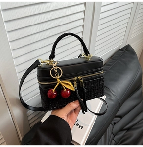 Detail of black tweed and leather handbag featuring a gold cherry charm and zipper