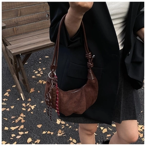 Détail du sac croissant en daim marron foncé avec nœud en cuir et breloque pompon