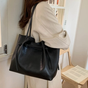 Detail of minimalist black oversized tote bag with decorative drawstrings on model shoulder