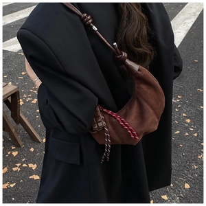 Vue de rue d'un sac demi-lune en daim marron foncé avec détails de glands tressés