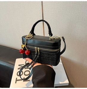 Detail of tweed and leather box bag featuring a plush handle and red cherry charm
