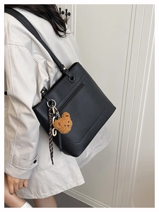 Close-up of black leather tote bag with a plush bear charm and decorative silk scarf