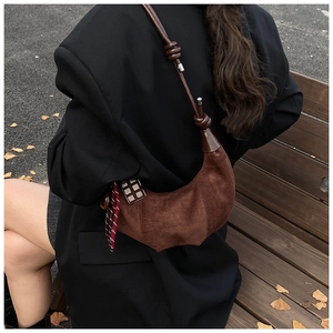Détail du sac demi-lune en daim marron avec nœuds décoratifs et pendentif à carreaux