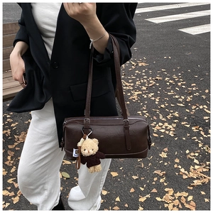Detail of dark brown vintage Boston bag featuring a plush bear charm on autumn street