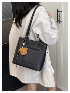 Detail of black pebbled leather tote with plush bear charm and ribbon on shoulder strap