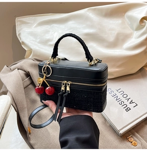 Detail of black leather and tweed texture handbag with dual zippers and red cherry charm
