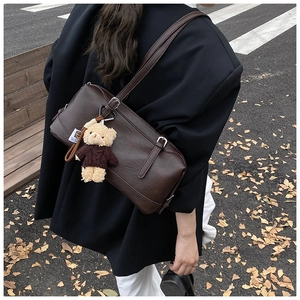 Detail view of deep brown vintage tote bag with bear charm on a park bench