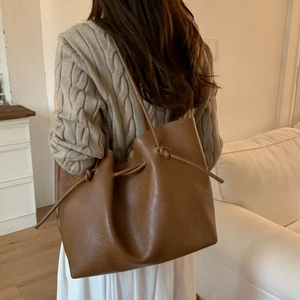 Detail of a brown leather tote bag with knot drawstrings and minimalist soft texture