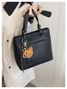 Close-up of black lychee texture tote bag with brown bear charm and striped ribbon