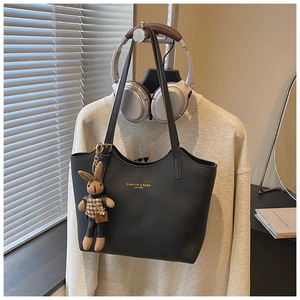 Détail d'un sac cabas en cuir noir avec un charm lapin à carreaux et lettrage doré chic