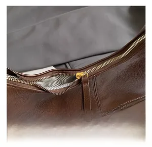 Detail of dark brown lychee leather texture and golden zipper with herringbone lining
