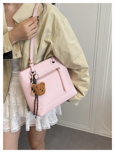 Detailed view of pink leather tote bag featuring a cute brown teddy bear charm and side zip pocket