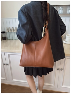 Close-up of caramel brown leather tote bag with colorful wooden bead charm on strap