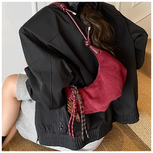 Détail du sac demi-lune bordeaux en daim avec pompon tressé et bandoulière nouée