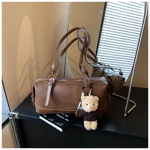 Close-up of retro brown barrel bag with smooth PU leather texture and cute bear pendant