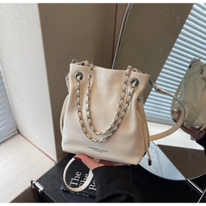 Detail view of cream bucket bag with silver chain handle and shoulder strap on a mirror