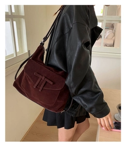 Detail of burgundy suede shoulder bag with T-shaped leather strap on black jacket