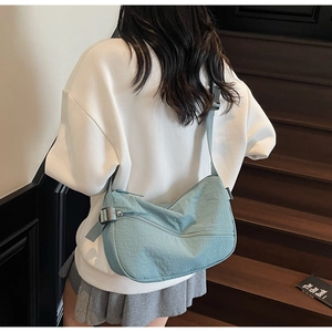 Lifestyle view of light blue nylon crescent bag worn on wooden stairs with casual outfit