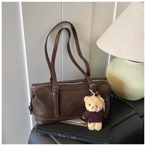 Detail of a dark brown retro barrel bag featuring a plush bear charm and silver zipper